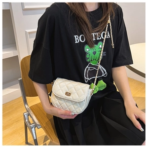 Detail of white quilted crossbody bag with gold twist lock and chain strap on model