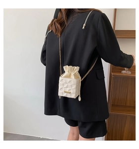 Detail of cream quilted bucket bag with gold chain strap on black blazer outfit