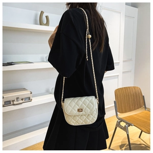 Detail of a quilted crossbody saddle bag with gold chain strap and spherical buckle