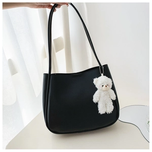 Detail of black matte tote bag with a cute white plush bear charm on minimalist background