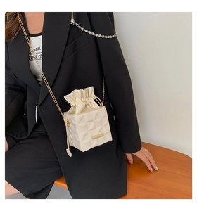 Detail of white geometric bucket bag with drawstring closure and golden chain strap