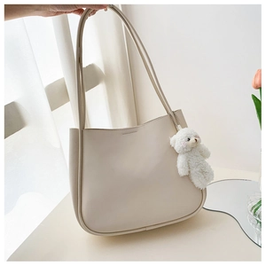 Detail of beige soft leather tote bag with plush bear charm and long shoulder strap