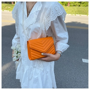 Detail of bright orange crossbody bag with V-quilted texture and white pearl strap
