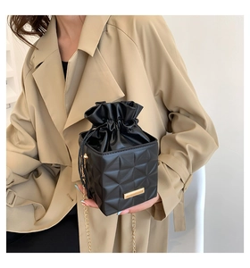 Detail of a black cube bucket bag with geometric quilted pattern and gold chain strap