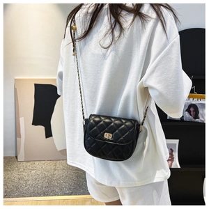 Detail of black quilted leather saddle bag with gold chain strap worn by a model