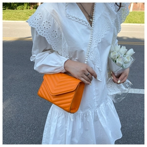 Detailed view of an orange chevron quilted crossbody bag with stylish pearl strap