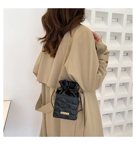 Detailaufnahme einer schwarzen Stepptasche mit goldener Kette auf einem Khaki-Mantel