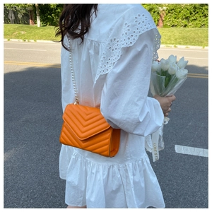 Detail of bright orange quilted crossbody bag with stylish white pearl chain strap