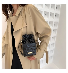 Detail of black quilted bucket bag with golden chain strap on a trench coat