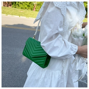 Green crossbody bag with V-quilted texture and pearl chain strap worn by a model