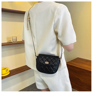 Close-up of black quilted leather saddle bag with golden twist lock and chain strap