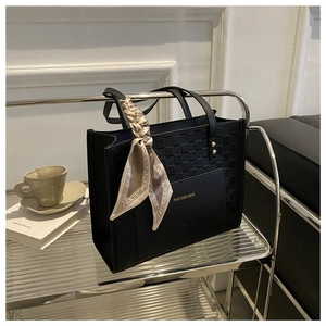 Detail of black tote bag with woven texture, smooth leather finish and decorative silk scarf