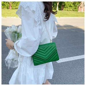 Close-up of green quilted shoulder bag with white pearl chain strap on a white dress