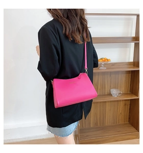 Detail of fuchsia leather crossbody bag with gold logo on a black suit backdrop