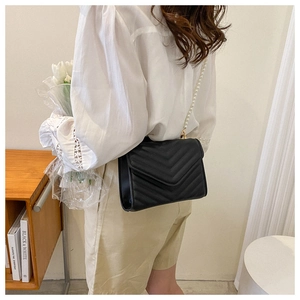 Detail of black quilted crossbody bag with pearl and gold metal chain strap on model