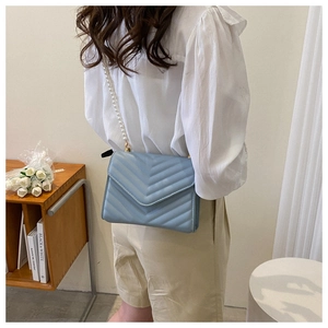 Close-up of light blue crossbody bag with chevron quilting and elegant faux pearl chain strap