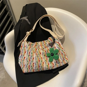 Colorful bohemian knit tote bag with beige strap and large flower charm on a black blazer