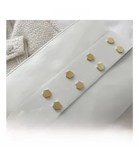 Macro view of white leather bag featuring golden hexagonal rivets and precise stitching