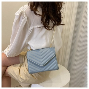 Detail of light blue crossbody bag featuring V-shaped quilting and pearl bead strap