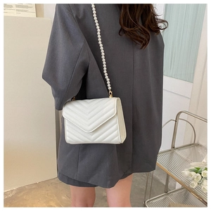 Detailed look of white quilted crossbody bag with pearl strap on gray blazer outfit