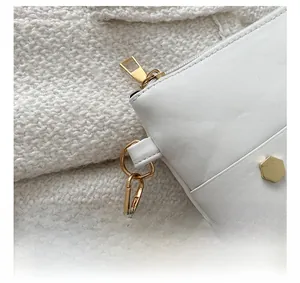 Close-up of golden hardware hooks and hexagonal metal buckle on white leather bag