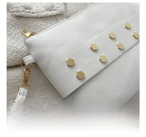 Close-up of white leather texture with golden hexagonal rivets and zipper detail