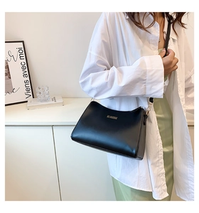 Detail of minimalist black leather shoulder bag featuring a sleek gold logo and metal zipper
