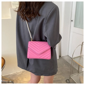 Detail of pink chevron quilted crossbody bag with elegant white pearl strap on model