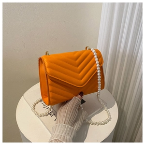 Detail of orange quilted crossbody bag featuring a stylish white pearl chain strap