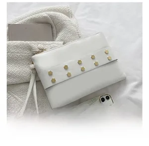 Detail view of white leather envelope bag featuring gold hexagonal studs and wrist strap