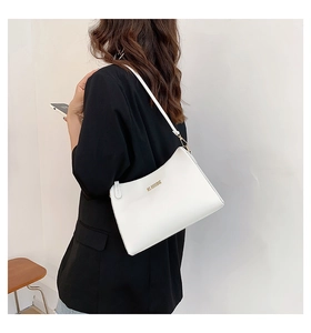 Detail of white leather shoulder bag with gold lettering shown on a model in a black suit