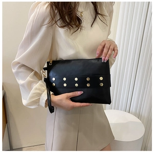 Close-up of black rivet clutch bag with gold hexagonal studs and wrist strap