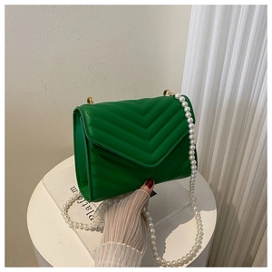 Detail of green quilted leather crossbody bag with V-shaped texture and pearl chain