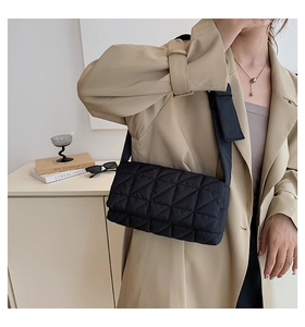 Detailed view of a black quilted crossbody bag worn over a stylish khaki trench coat