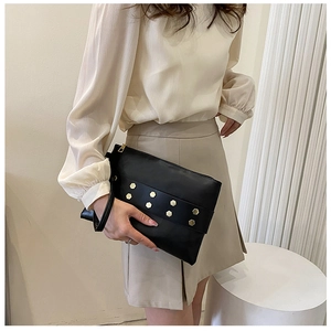 Detail of black leather clutch bag with golden hexagonal rivets and zipper closure