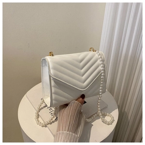 Detail of white quilted crossbody bag with pearl chain strap and elegant gold hardware