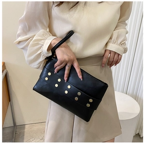 Detail of black matte faux leather clutch bag with golden hexagonal studs and wrist strap
