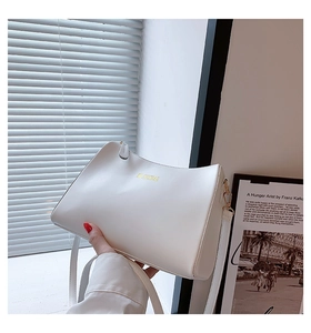 Close-up of white minimalist leather bag with gold brand logo and metal hook detail