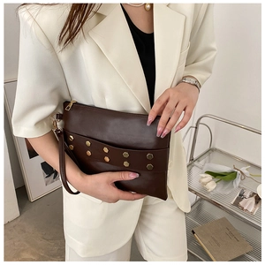 Detail of dark brown leather envelope clutch with golden hexagonal studs and wrist strap