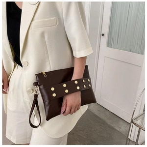 Detail of dark brown leather clutch featuring golden hexagonal rivets and wristlet strap