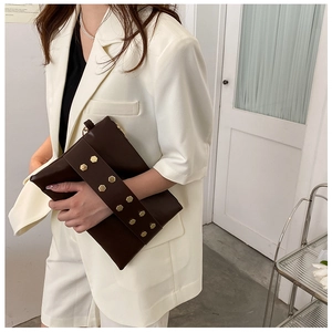 Detail of dark brown faux leather clutch featuring dual rows of gold hexagonal metal studs