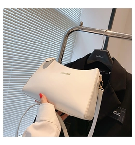 Close-up of a white minimalist shoulder bag with gold brand logo lettering held by a model