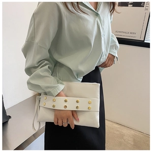 Close-up of white leather clutch bag featuring decorative gold hexagonal studs and wrist strap