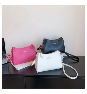 Three minimalist matte leather crossbody bags in magenta, black and white on a desk