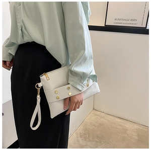 Detail of white leather clutch with gold hexagonal rivets and wrist strap held by model