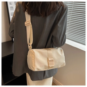 Close-up of a cream nylon cylindrical crossbody bag with wide strap on a model back