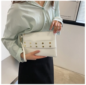 Detail of white leather envelope clutch featuring gold hexagonal studs and wrist strap