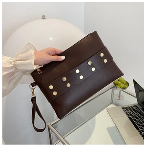 Close-up of dark brown matte leather envelope clutch bag with gold hexagonal rivets
