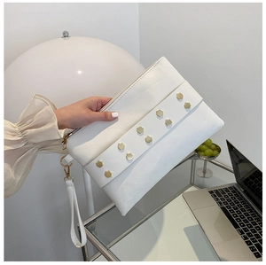Close-up of a white leather clutch bag featuring elegant gold hexagonal rivets and wrist strap