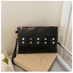 Close-up of black envelope clutch bag with gold hexagon rivets and a side wrist strap